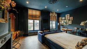 A modern bedroom with a large bed, a seating area, a dining table, and a view of the city through large windows. - Hotel 1635 (Haarlem)