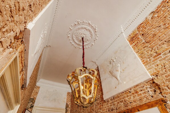 A chandelier in a room with exposed brick walls and ornate ceiling details. - Hotel 1635 (Haarlem)