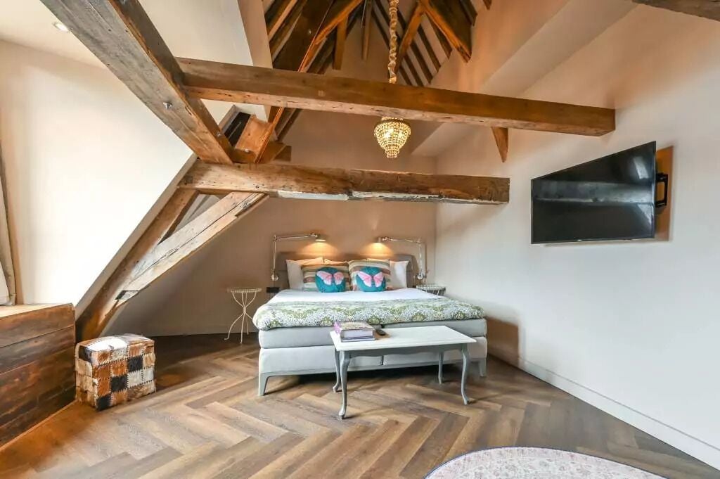 A bedroom with a wooden ceiling, a bed with a floral bedspread, a bedside table, and a wall-mounted TV.