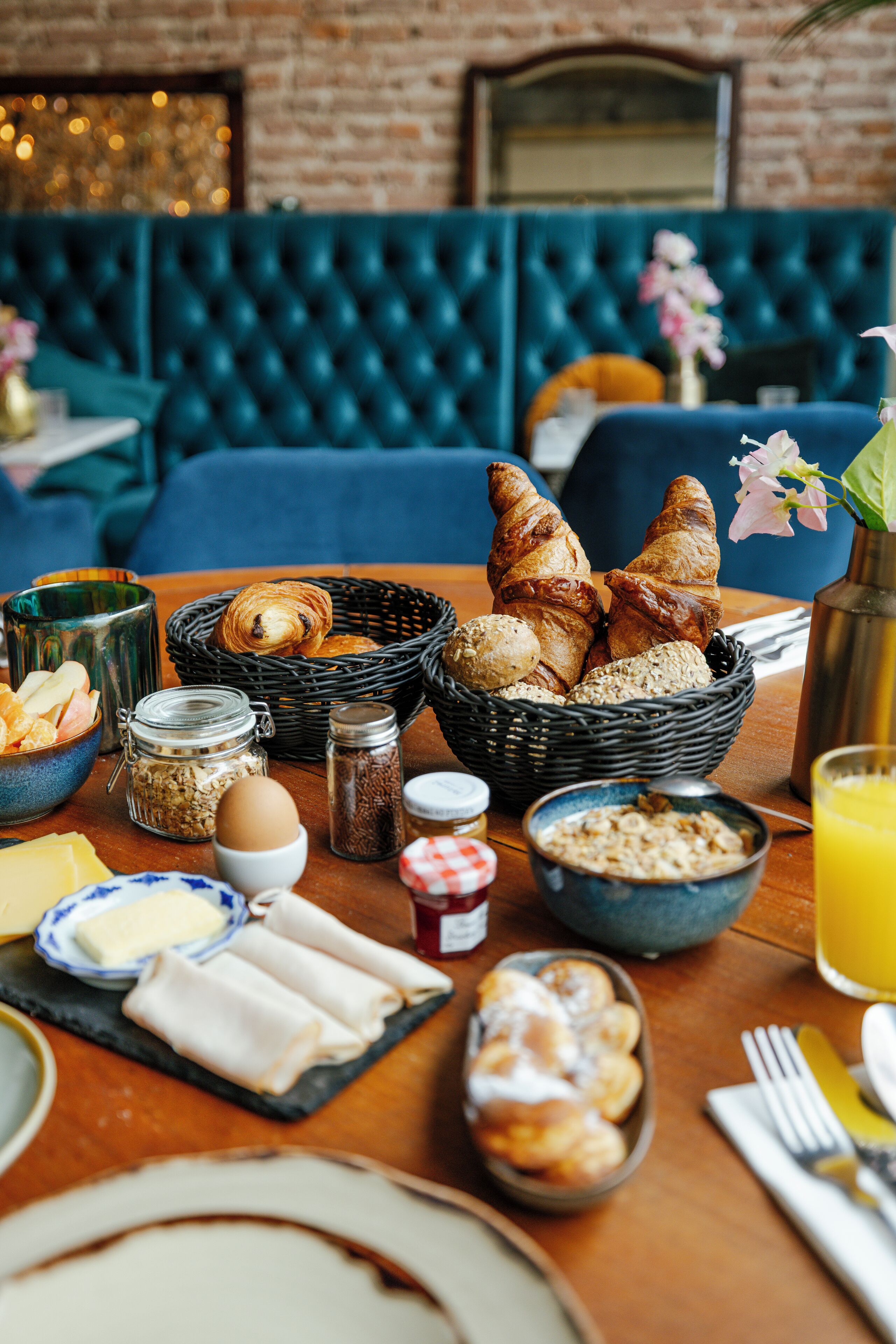 A breakfast table with croissants, bread, and pastries, along with condiments and a glass of orange juice.