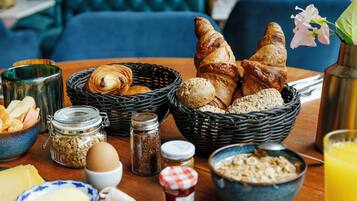 A breakfast table with croissants, bread, and pastries, along with condiments and a glass of orange juice.