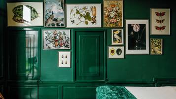 Ein Zimmer mit grünen Wänden, einem Bett mit grüner Bettdecke und verschiedenen gerahmten botanischen und Insektenabbildungen an der Wand.