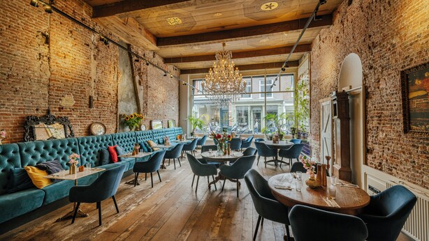 A restaurant with a brick wall, wooden ceiling, and a large chandelier. There is a green sofa and multiple tables with chairs. - Hotel 1635 (Haarlem)