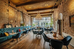 A restaurant with a brick interior, wooden floors, and a mix of seating arrangements including a blue sofa and round tables. - Hotel 1635 (Haarlem)