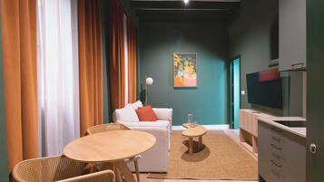 A modern living room with a sofa, two chairs, a small round table, a TV, and a painting on the wall.