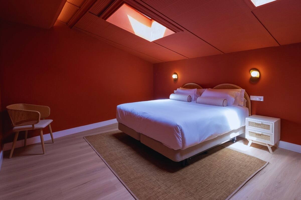 Une chambre à coucher comprenant un lit, une chaise, une table de chevet et une lucarne.