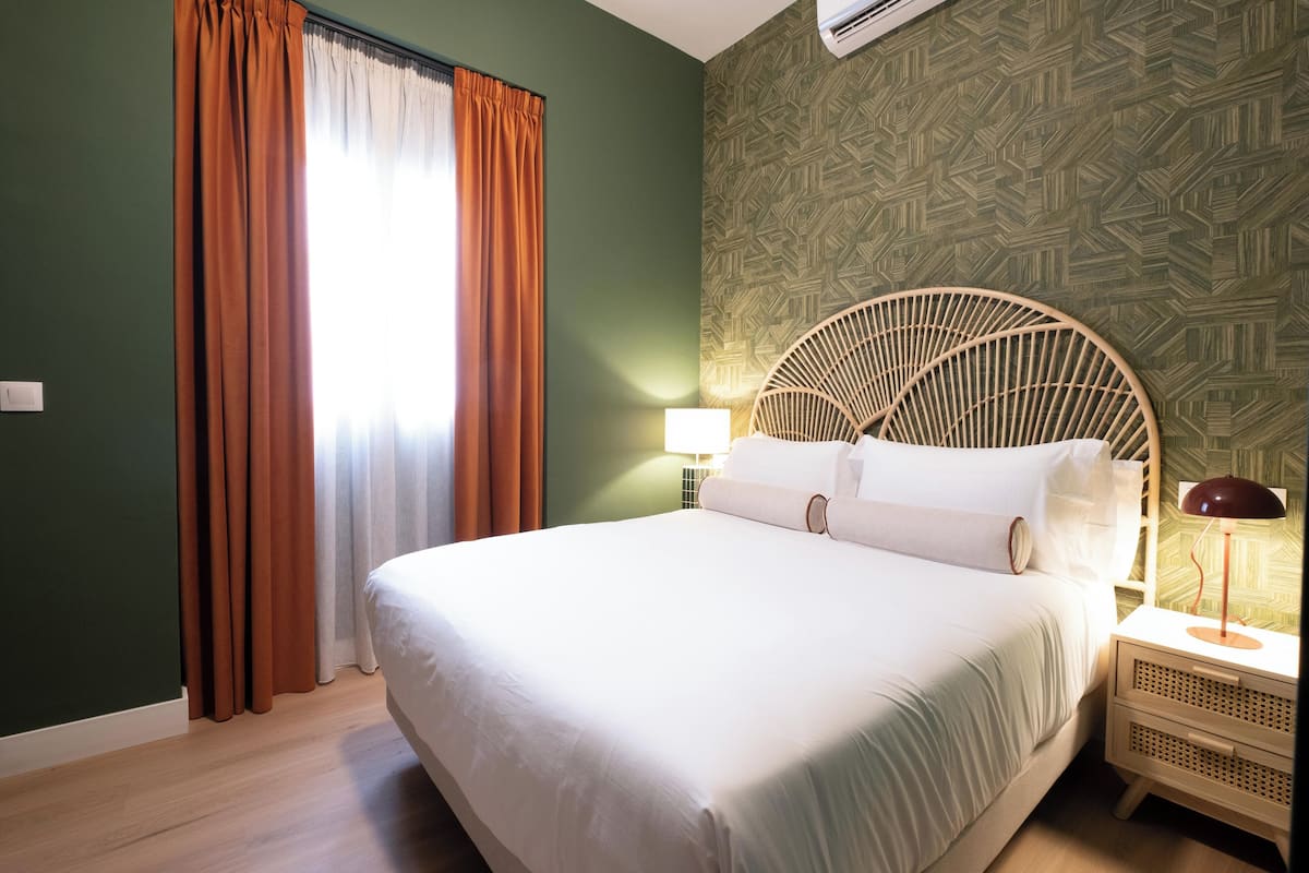 Une chambre d’hôtel avec un grand lit, une tête de lit en bois, une table de chevet avec une lampe et un papier peint à motifs.