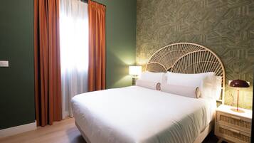 A hotel room with a large bed, a wooden headboard, a nightstand with a lamp, and a patterned wallpaper.