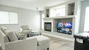 A modern living room with a sofa, armchairs, a coffee table, a fireplace, and a television displaying a movie.