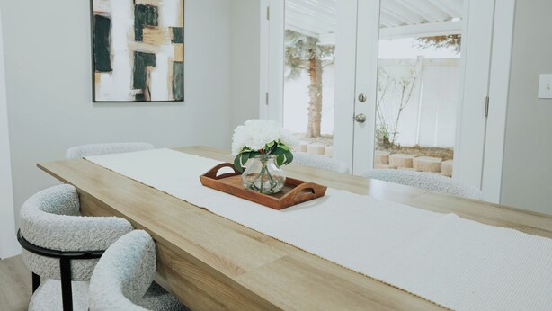A modern dining area with a wooden table, white chairs, and a vase with white flowers.