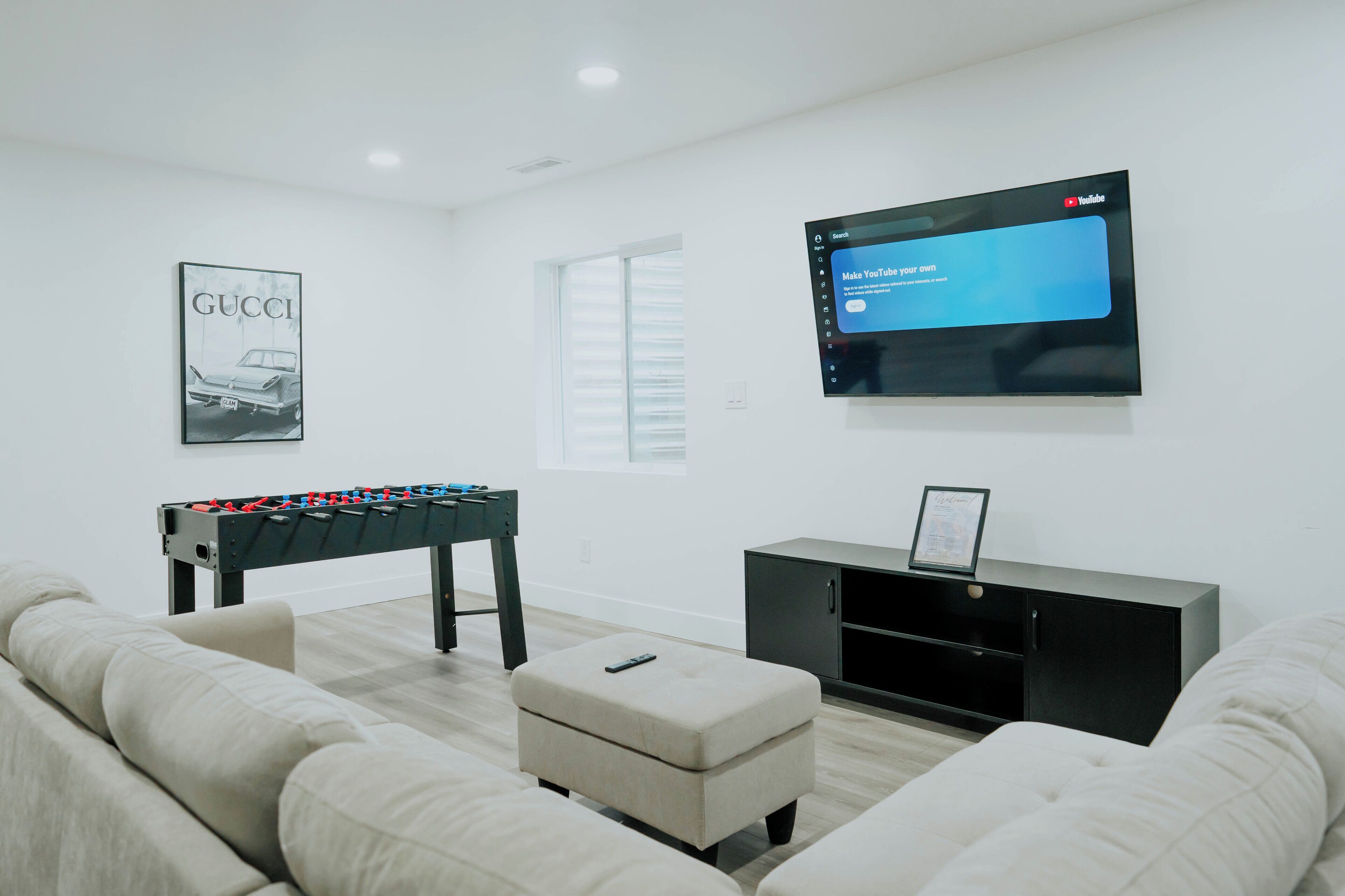 A modern living room with a foosball table, a flat-screen TV mounted on the wall, and a framed certificate on a black cabinet.