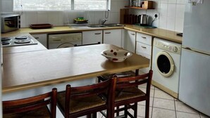 Une cuisine avec un îlot central, un lave-linge et une fenêtre avec des stores.