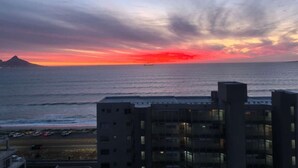 Une vue sur le coucher de soleil en bord de mer, avec des bâtiments au premier plan.