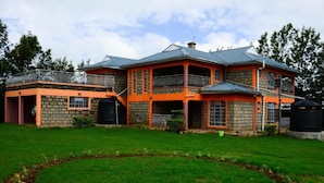 Una casa grande de varios pisos con fachada de piedra y detalles en naranja, con varios balcones y un amplio jardín delantero.
