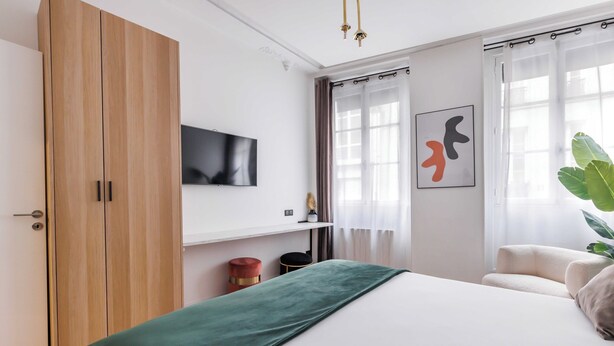 A bedroom with a bed, a TV mounted on the wall, a plant, and a window with curtains. - Charming Duplex - 2br/6p - Saint Germain (Paris)
