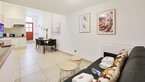 Un salon moderne avec un canapé gris, un coin repas avec une table et des chaises, et une cuisine en arrière-plan.
