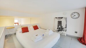 Une chambre d’hôtel moderne avec un grand lit, une petite table ronde, une horloge et une œuvre d’art murale.