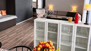 A modern living room with a sofa, a white console table with glass doors, and a dining area with a wooden table and chairs.