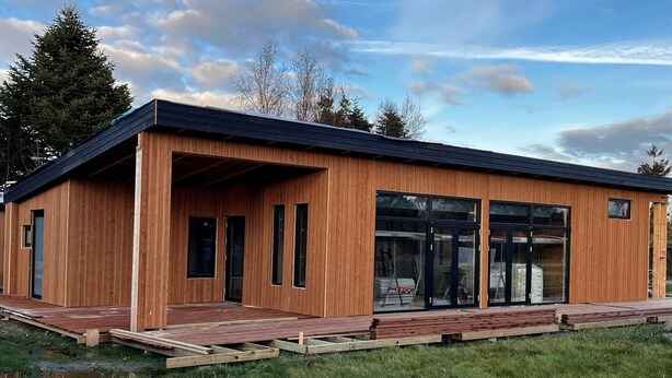 A modern wooden building with large glass windows and a covered entrance area.