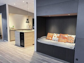 Een modern interieur met een keukenhoek, een ingebouwde bank met kussens, en een wand met horizontale latten.