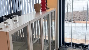A room with a white console table, a red vase, and two glasses.