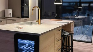 A modern kitchen with a central island, pendant lights, and a view of a snowy landscape through a glass door.