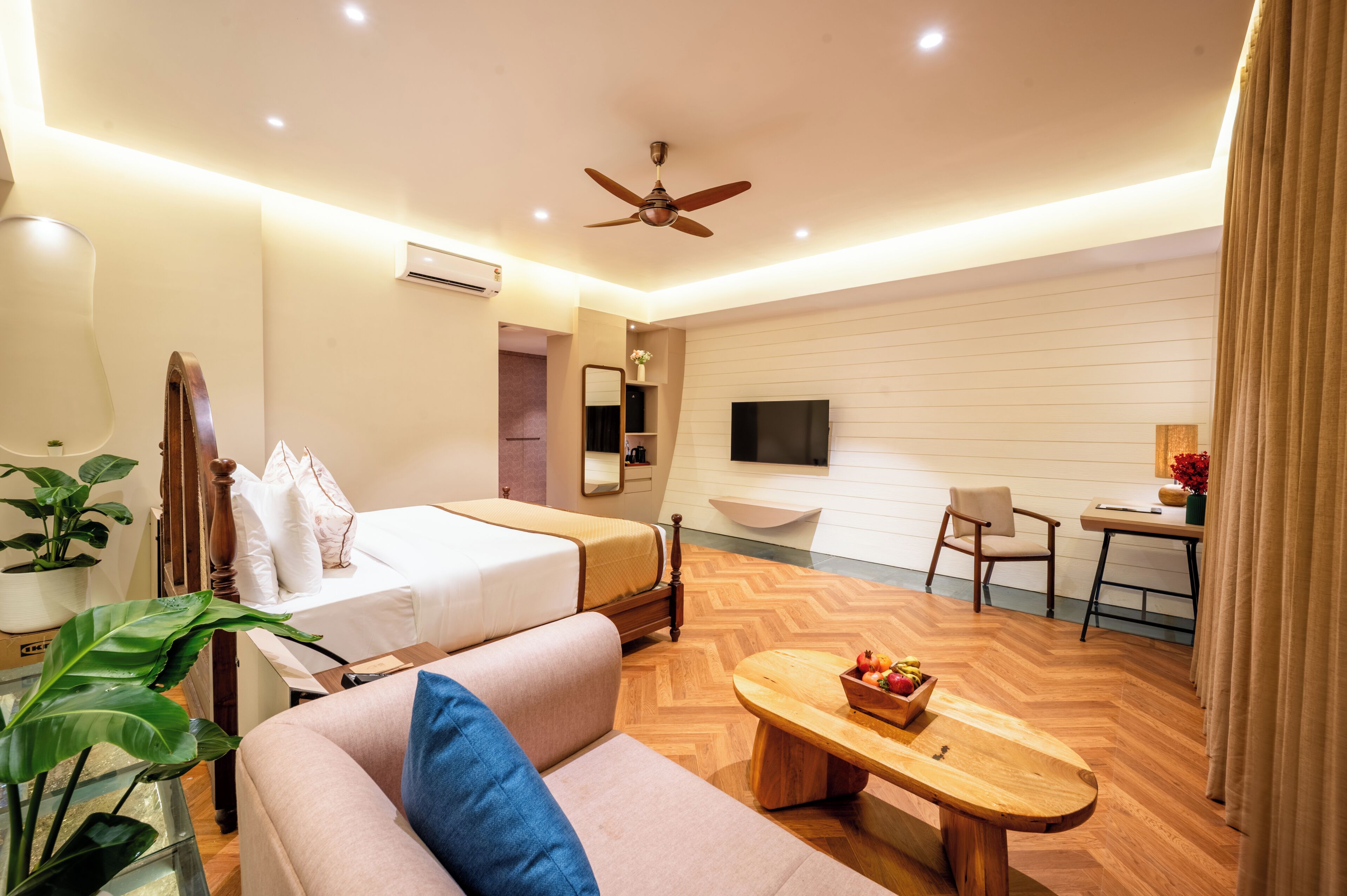 Habitación de hotel con cama, sofá, escritorio, silla, televisión y ventilador de techo.