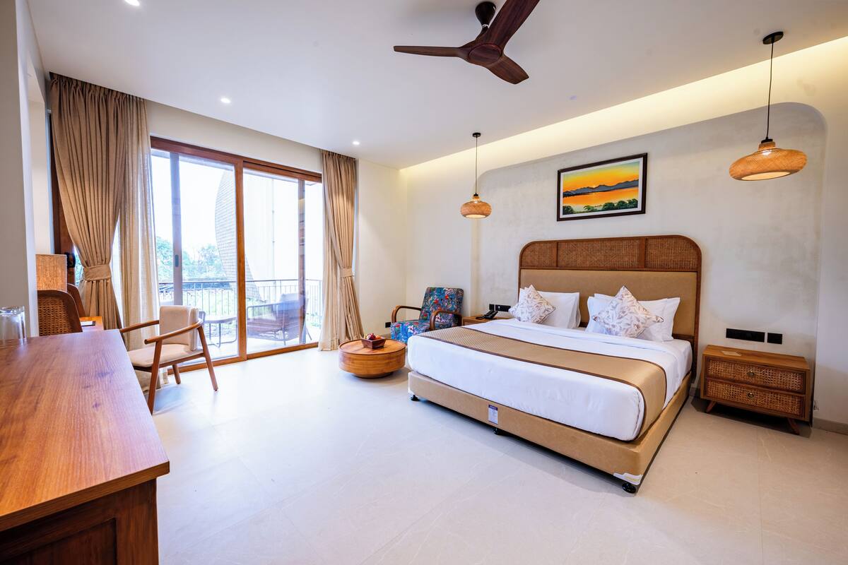 Une chambre d’hôtel moderne dotée d’un grand lit, d’une table à manger, d’une chaise, d’un ventilateur de plafond et d’une grande fenêtre avec des rideaux.