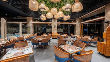 A restaurant interior with wicker furniture, hanging lights, and a stone accent wall.