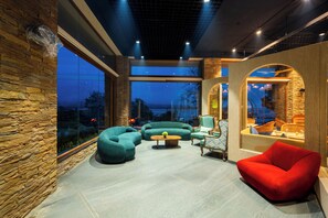 Ein modernes Interieur mit Steinwänden, großen Fenstern und einer Sitzecke mit Sofas und einem roten Sessel.