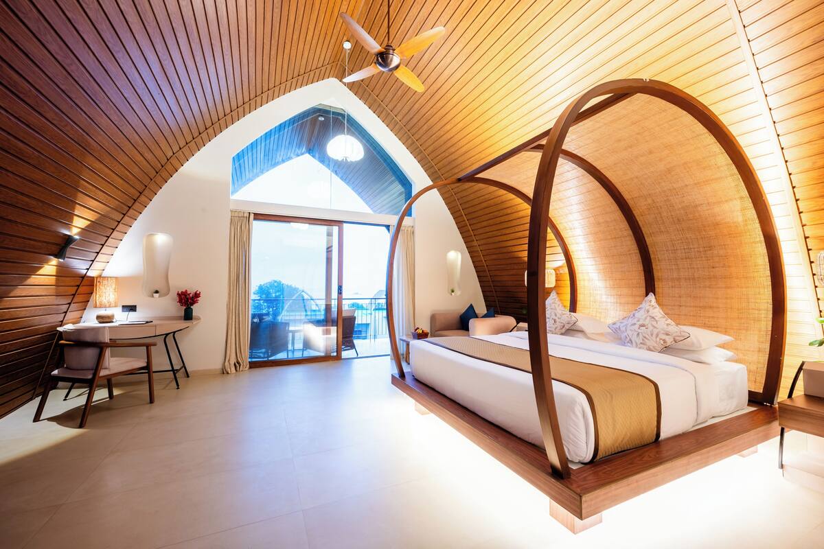 Une chambre à coucher avec un plafond incurvé, un lit, un bureau et une vue sur l’extérieur.