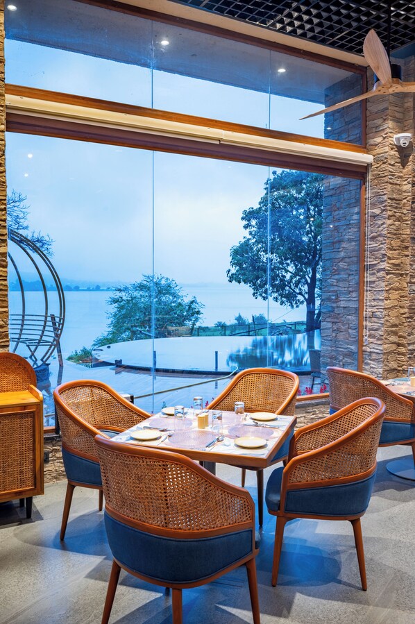A dining area with wicker chairs and a table set for four, overlooking a body of water and trees.