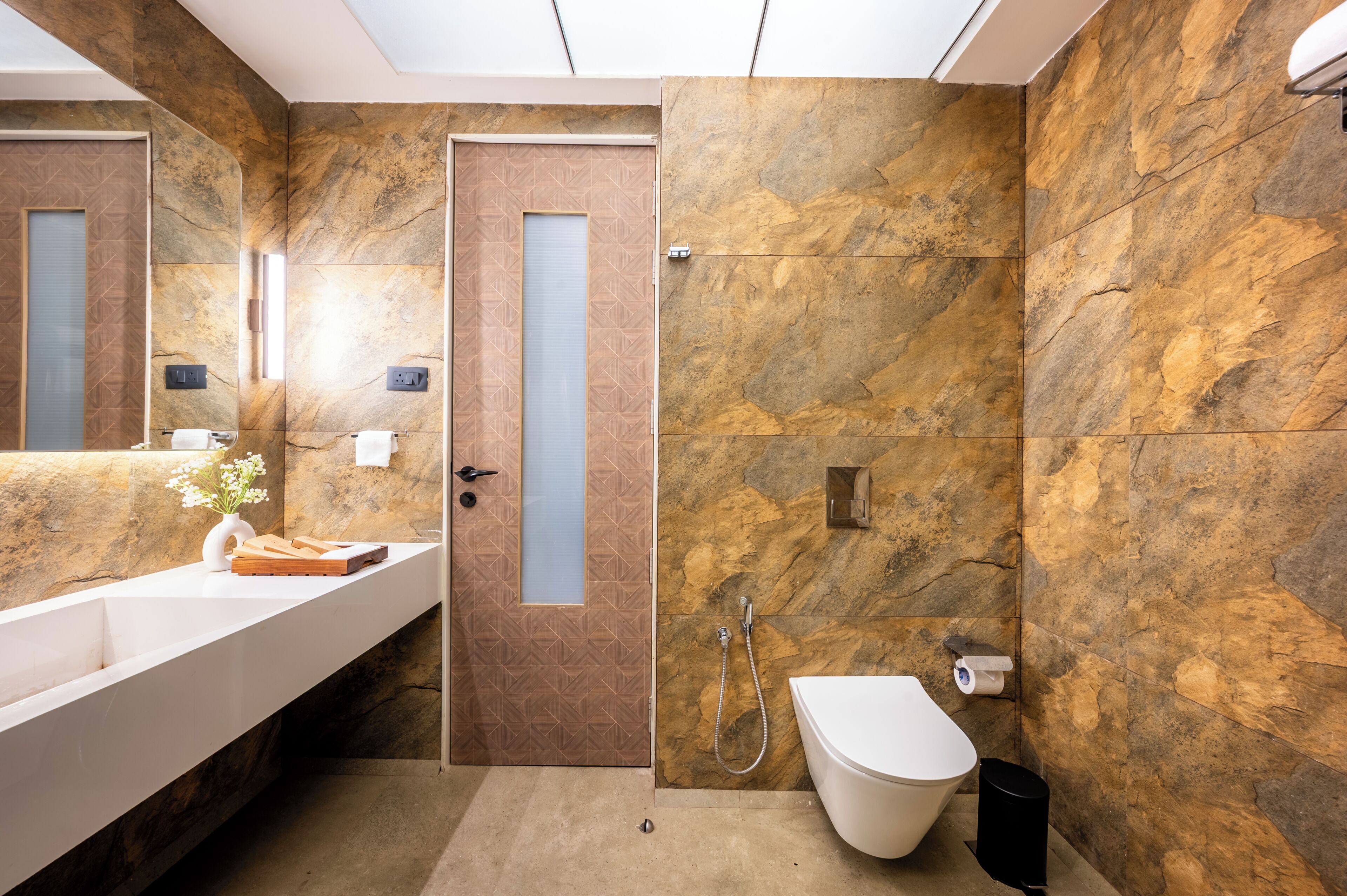 A modern bathroom with a marble wall, a white sink, and a shower area.
