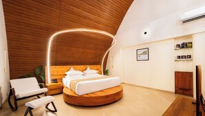A modern bedroom with a curved ceiling, a round bed, a wooden nightstand, a bench, and a TV. - ARK Lake Resort (Igatpuri)