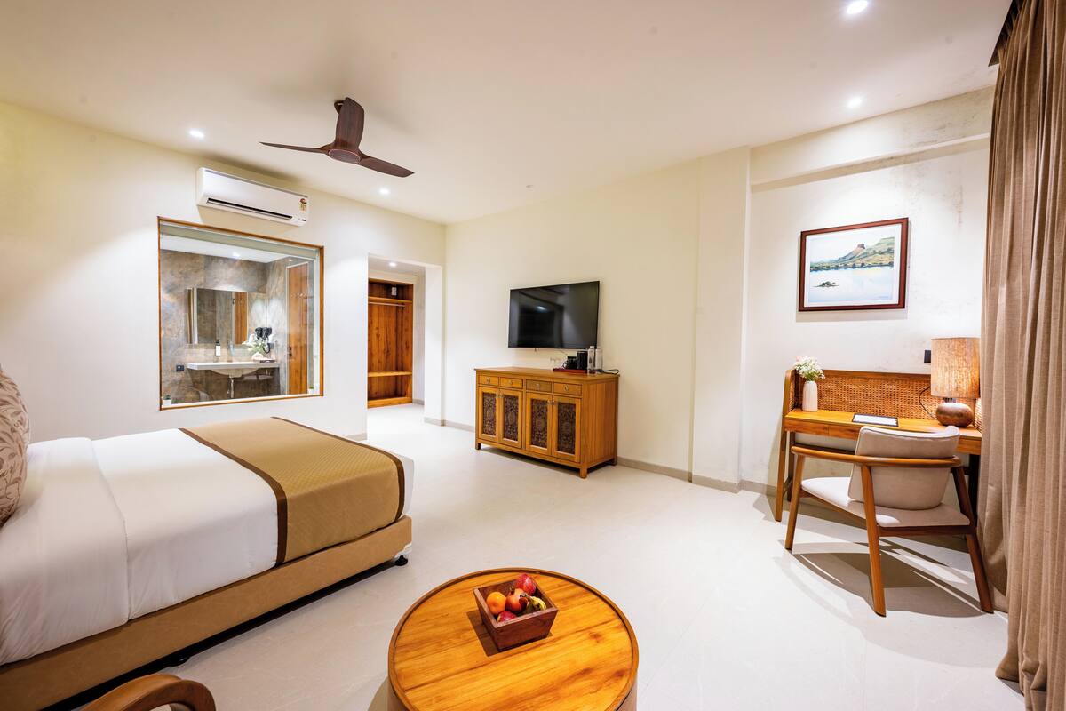 Une chambre d’hôtel comprenant un lit, une télévision, un bureau avec une chaise, une armoire en bois et une table basse ronde.