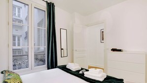 Una camera d'albergo con un letto, una finestra con tende, un comò e uno specchio.