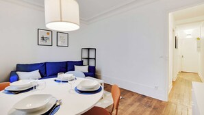 Un'area pranzo con un tavolo rotondo apparecchiato per quattro persone, un divano blu e una lampada a soffitto bianca.