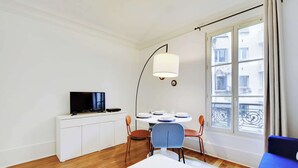 Un soggiorno moderno con un tavolo da pranzo apparecchiato per quattro persone, una televisione su un mobile bianco e un'ampia finestra con vista sugli edifici.