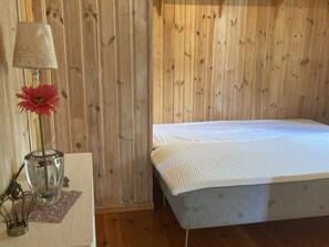 Une pièce aux murs lambrissés, avec un lit simple, une lampe et un vase contenant une fleur.