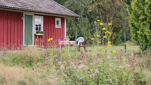 Una casa de madera roja con una puerta verde, un ventanal pequeño y una mesa con mantel rosa.