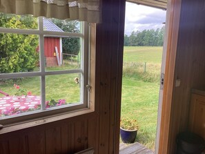 A wooden door leading to a garden with a red shed, a table with pink flowers, and a potted plant. - 4 Person Holiday Home in Torup (Torup)