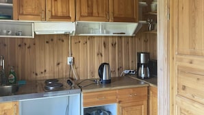 Cocina compacta con armarios de madera, estufa, cafetera y hervidor.