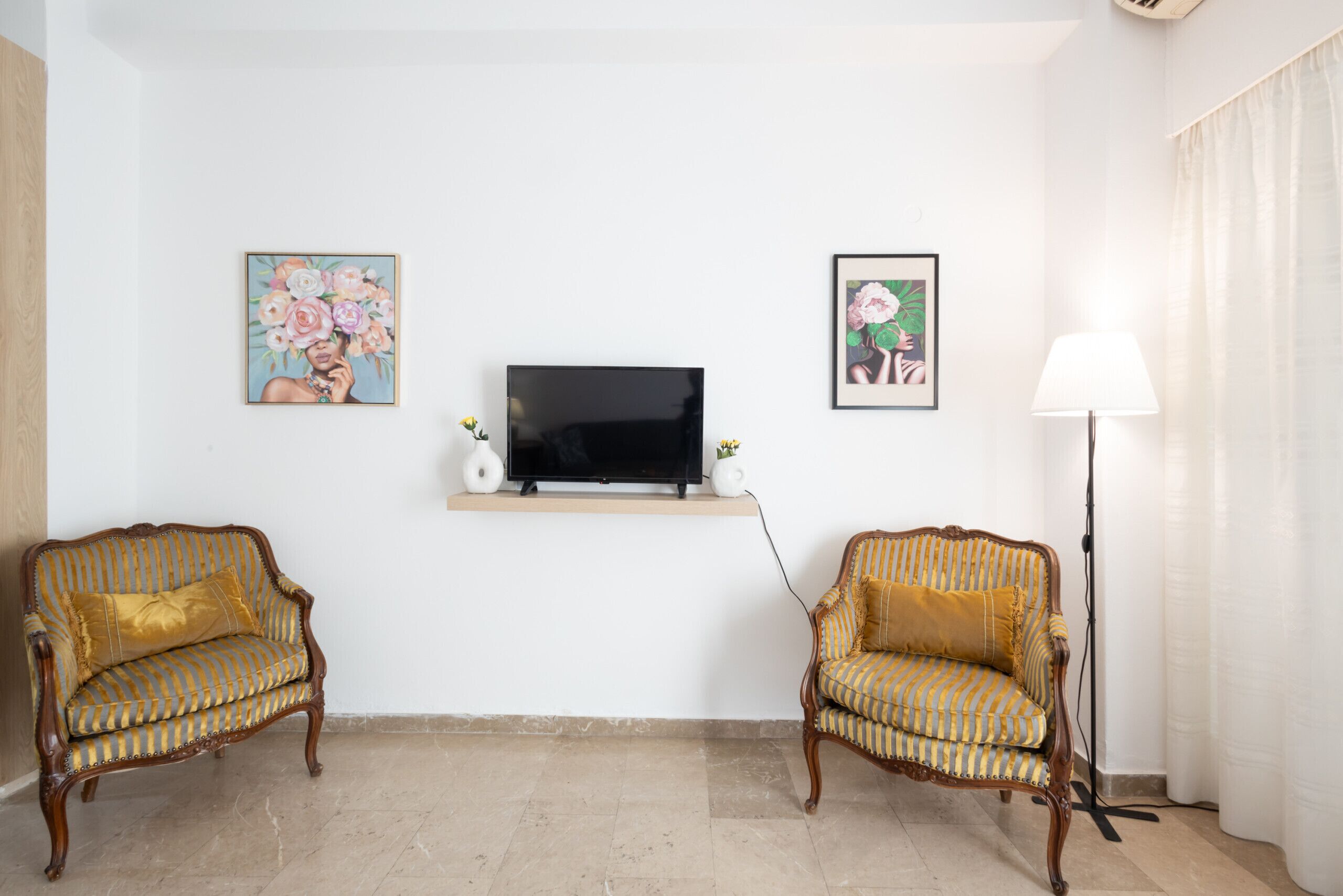 Een woonkamer met twee fauteuils, een televisie op een plank, en kunstwerken in lijsten aan de muren.
