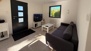 Un salon moderne doté d’un téléviseur à écran plat, d’un canapé, d’une table basse et d’une fenêtre donnant sur un paysage verdoyant.