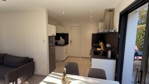 Un espace de vie moderne comprenant un canapé, une table à manger avec une bouteille, et un coin cuisine équipé d’un four à micro-ondes et d’une cuisinière.