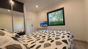 Une chambre à coucher avec un lit, une télévision, une armoire et une fenêtre donnant sur un arbre.