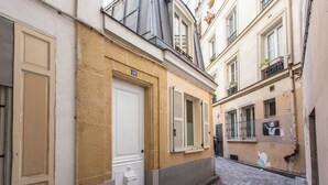 Una calle estrecha flanqueada por edificios, con una puerta blanca y ventanas con contraventanas.