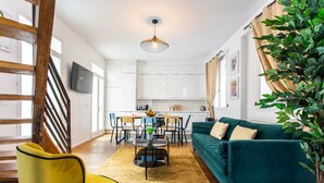 Una sala moderna con un sofá verde azulado, un sillón amarillo y una zona de comedor con mesa y sillas de madera.