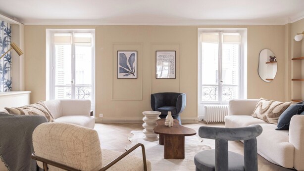 Amplia sala de estar con dos sofás blancos, un sillón azul y una mesa de centro redonda de madera.