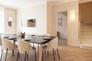 Un coin repas avec une table dressée pour six personnes, six chaises, un miroir, un tableau encadré et un escalier.